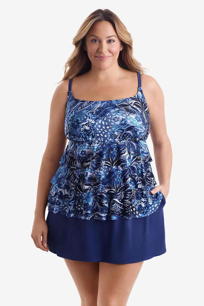 Woman wearing a tiered one-piece swimsuit with an abstract blue pattern with her hand in pocket