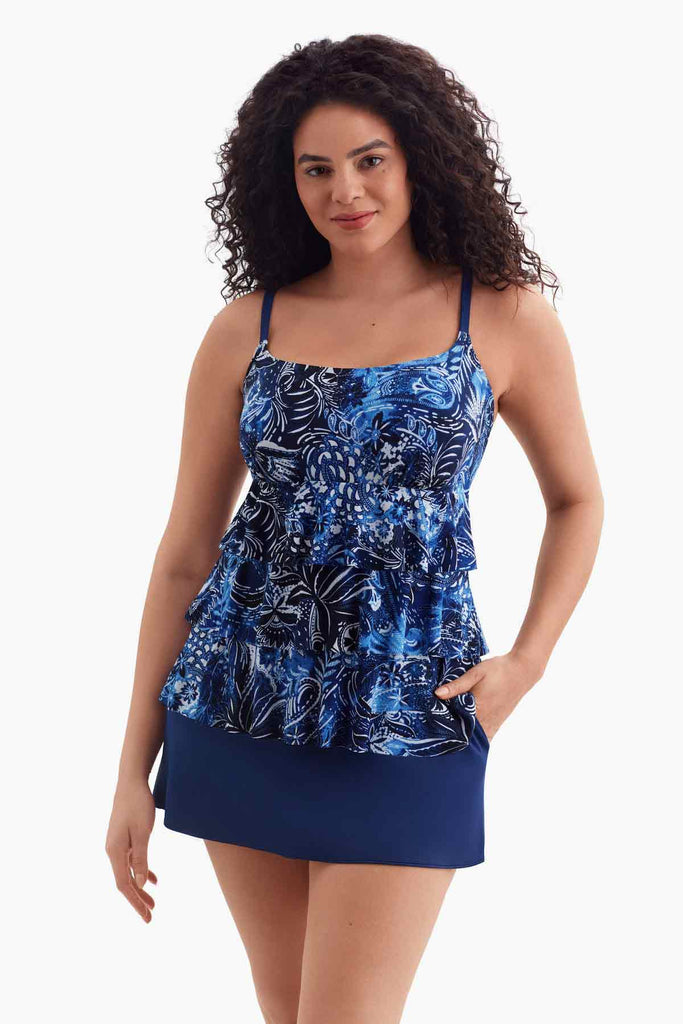 Woman wearing a tiered one-piece swimsuit with a blue abstract floral print with hand in pocket